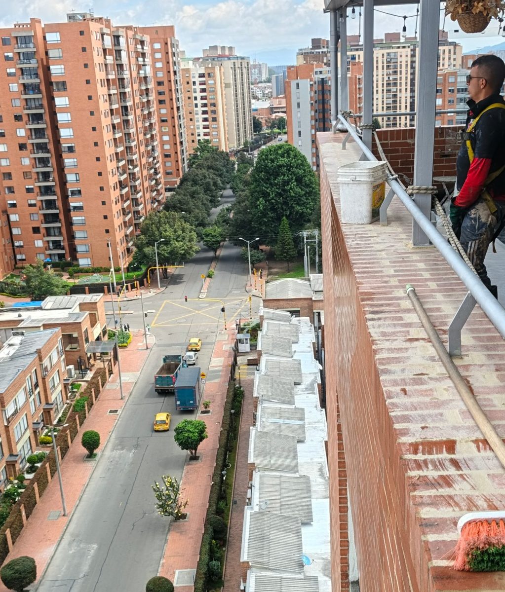 Técnico con arnés y línea de vida revisando la fachada desde la azotea